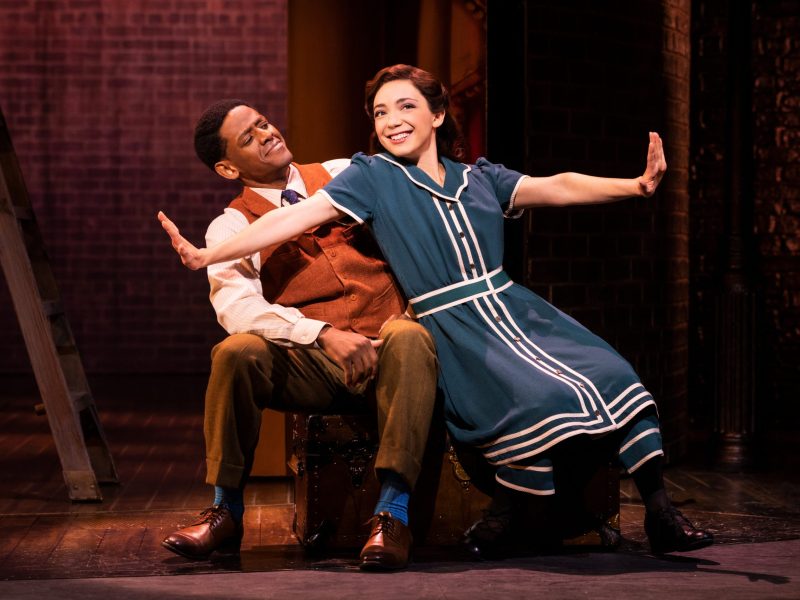 two adults on a bench, woman on right with arms out, smiling, leaning to her right on man to her left