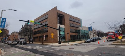 A four-story brick building with large windows sits at the corner of an intersection.