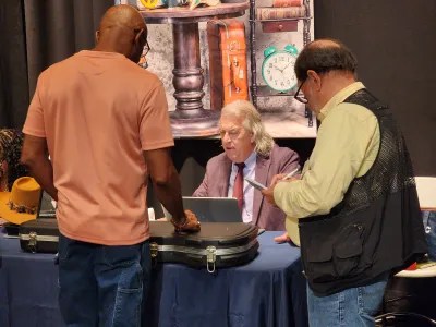 man seated at table with two man standing on other side of table