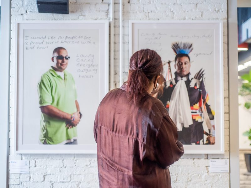 person in maroon shirt looks at two photos on a white wall of a gallery