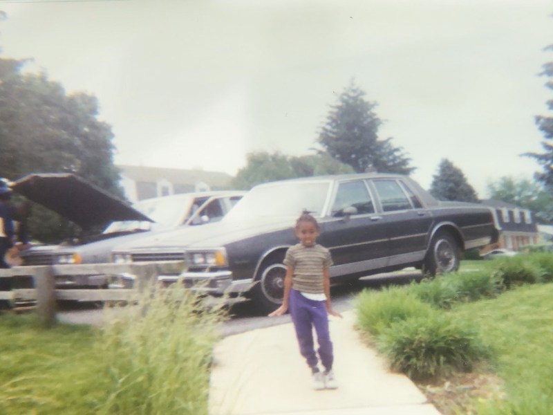 Author Jalynn Harris, as a young child, stands in front of her parents' matching silver cars.