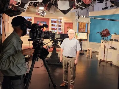 two men, one cameraman filming another on a tv studio set