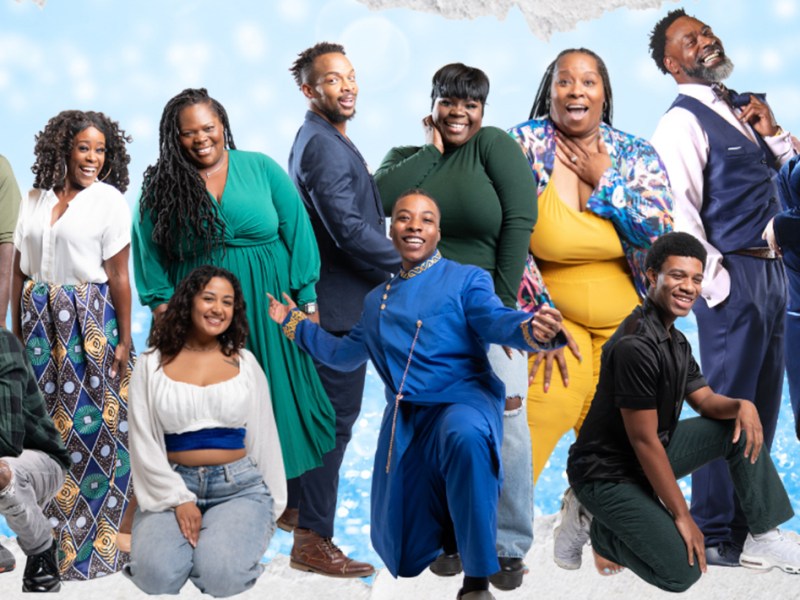 Group of 20 or so people standing and kneeling against blue backdrop and smiling