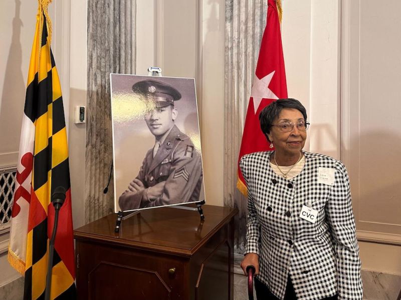 WASHINGTON - Joann Woodson, of Clarksburg, Maryland, stands next to the portrait of her late husband, Army Staff Sgt. Waverly Woodson Jr., who on Tuesday was posthumously awarded the Distinguished Service Cross by the Army for his gallantry on D-Day in 1944. (Katharine Wilson/Capital News Service)