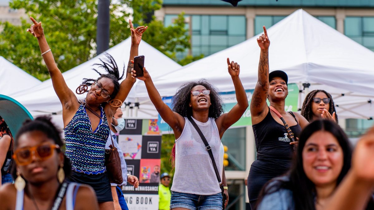 Three women dancing outside with their hands in the air