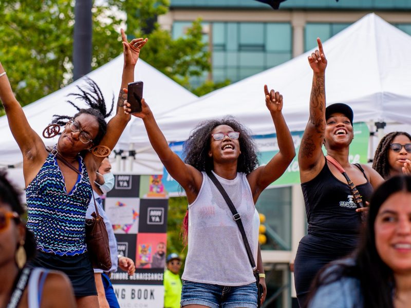 Three women dancing outside with their hands in the air