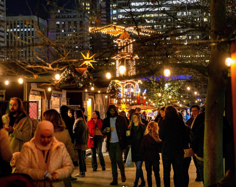 crowd of people walking at night along a promenade lit with holiday lights