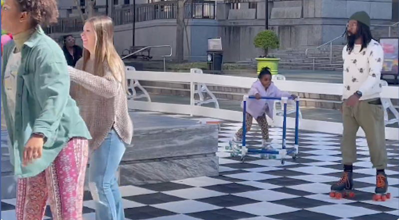 3 adults and 1 child roller skating on a black and white checkered floor outside