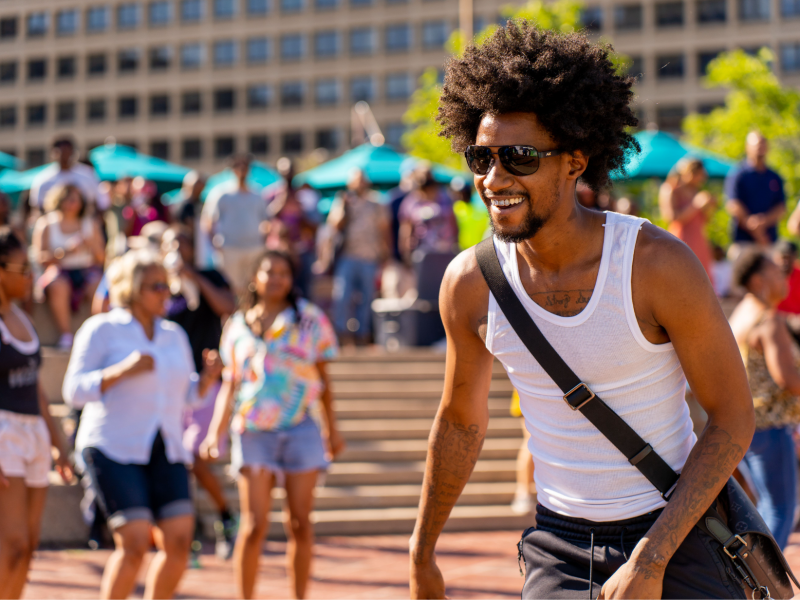 man with afro, goatee, and sunglasses in white tank top smiling at the Inner Harbor Amphitheater