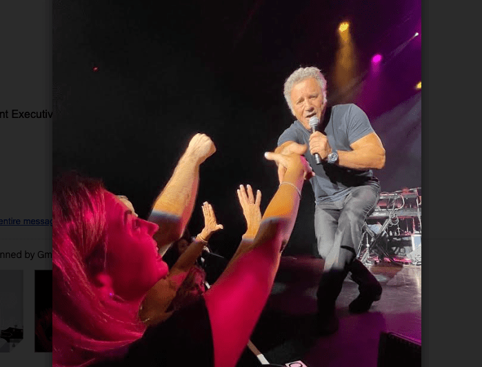 Man in gray tshirt and microphone reaching to woman in audience to shake her hand