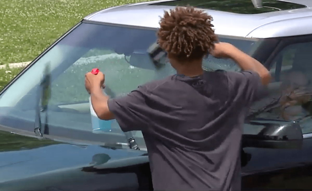 Screenshot of young boy from behind cleaning the windshield of a car