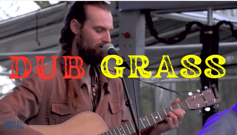 man with slicked back hair and beard and moustache playing guitar with microphone in front of him and the words "Dub Grass" printed across photo