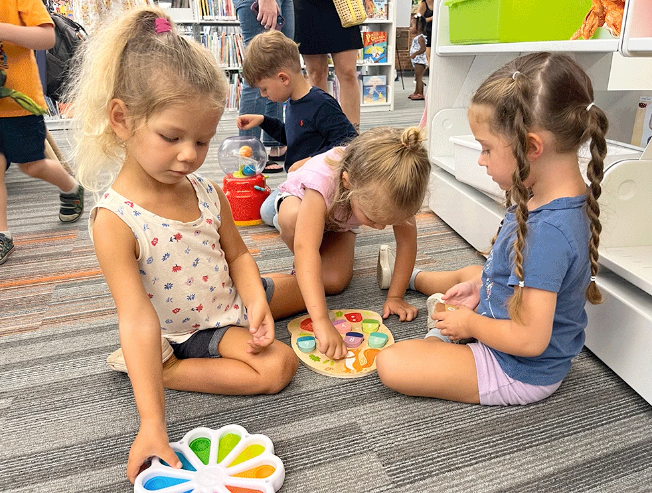 4 children sitting on the floor of a library playing games