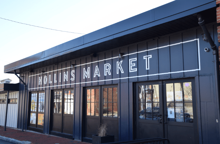 angled view of blue storefront with windows and Hollins Market written above windows