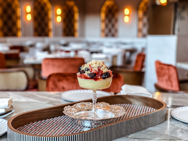 dessert on a tray in a restaurant with red velvet chairs and arches in the background