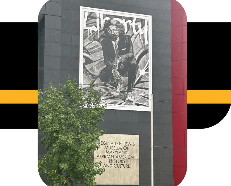 large banner of Frederick Douglass dressed in contemporary clothes, banner hanging from the side of a dark gray brick building