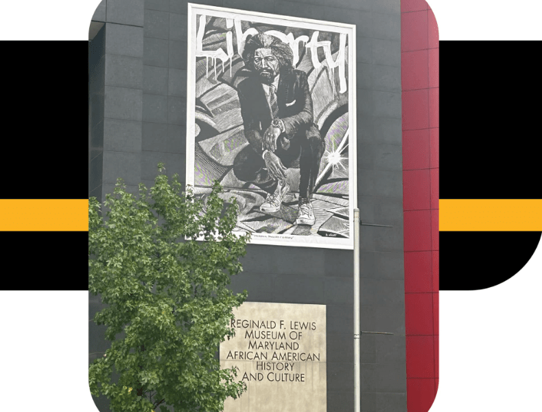 large banner of Frederick Douglass dressed in contemporary clothes, banner hanging from the side of a dark gray brick building