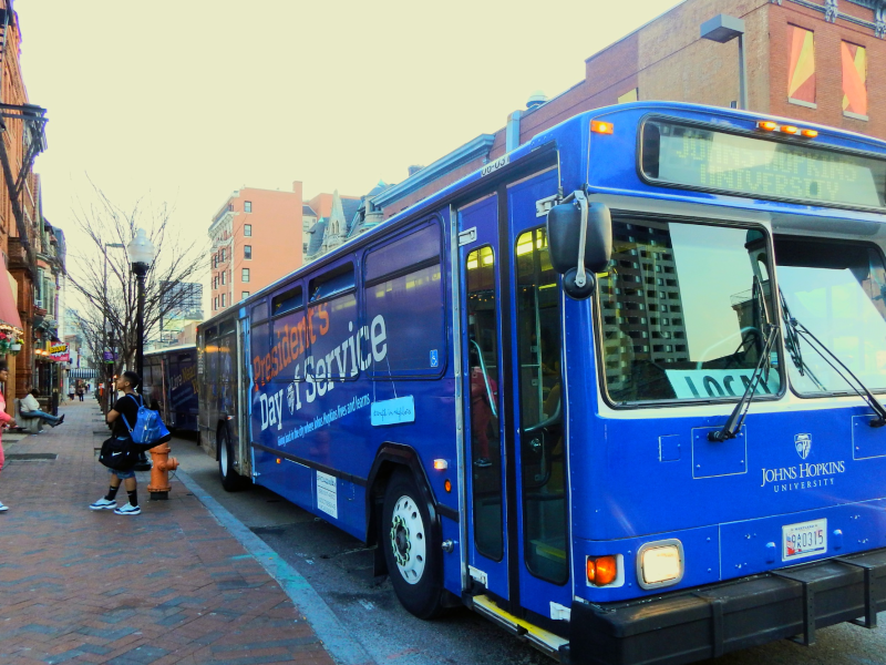 front angled view of blue jhu shuttle bus on a street next to a red brick building